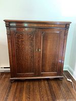 Front view of vintage wooden dresser cabinet with two closed doors, showing wood grain and carved top details.