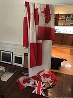 Five Canadian flags draped over a white panel, some folded, showing red and white maple leaf pattern, one Stars and Stripes partially visible on the floor, and a Union Jack flag also on the floor.