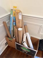 Cardboard box filled with multiple rolled posters and maps in tubes, showing size and packaging variety.