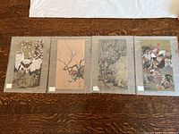 Four Asian scroll prints in protective envelopes, laid on wooden surface