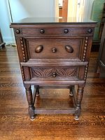 Front view of the vintage 2 drawer side table showing carved drawer fronts, round wooden knobs, beaded trim, turned legs, and glass top.