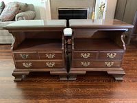 Front view of both matching hardwood side tables showing tops, open shelves, drawers with ornate metal pulls, and carved feet.