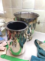 Two silver-plated ice buckets placed side by side on a kitchen counter. Smaller one in front and larger one behind.