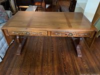 Front view of table showing walnut veneer top, two carved drawers with ring-pull hardware and trestle pedestal base