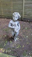 Front view showing the full statue of a boy holding a fish in a garden setting.