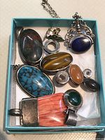 Box with assortment of 11 pieces of sterling silver jewelry including pendants and rings with various stones in blue, brown, orange, green colors.