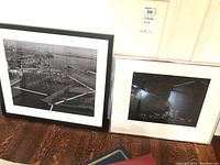 Two framed black and white photos placed side by side. The left photo shows an aerial daytime view of Toronto Harbour with docks, boats, and waterfront infrastructure. The right photo shows a night skyline of Toronto with city lights and buildings, including two illuminated towers.