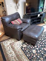 Photo of oversized brown leather armchair with striped pillow, viewed angled showing left side and front.
