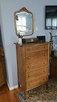 Front angled view showing full chest of drawers with four drawers and wood knobs, topped with small objects, and vintage wood-framed mirror hanging above.