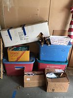 Stacked storage bins and boxes containing various Christmas decorations with one box labeled 'Jeco' containing two 3.5 ft table trees and a nutcracker doll sitting on top.