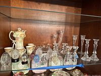 Shelf of various crystal candlesticks, porcelain pieces, and decorative eggs.