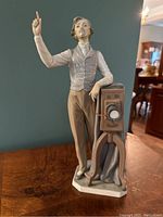 Front view of male photographer figurine with vintage camera on tripod, hand raised pointing.