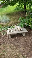 Outdoor concrete garden bench with animal figurines on top in a garden setting with grass and plants in the background.