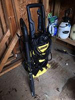 Full view of the Karcher power washer showing yellow and black body, wheels, handle, and coiled black hose.