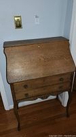Front view of vintage wooden secretary desk with closed fold-down surface and two visible drawers
