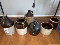 All six stoneware crocks and jugs arranged on a floor showing variety in shape and glaze