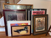 Seven framed wall art pieces and one empty picture frame arranged on the floor, showing a variety of frames and artwork including birds, festival poster, and botanical designs.