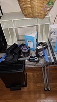 Overview of the lot showing two Jam Classic Bluetooth speakers in packaging, two digital cameras, Reolink E1 Pro camera box, and accessories on glass table.