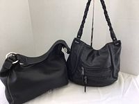 Two black leather purses displayed side by side, left hobo bag, right slouchy shoulder bag