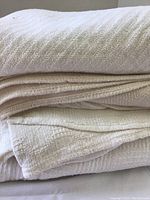 Four folded blankets stacked, showing various woven textures in off-white and cream shades.