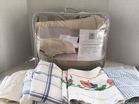 Photo showing the tan king size down alternative blanket packaged in a clear zippered bag with a label and four sets of king pillowcases laid in front in various patterns and colors.