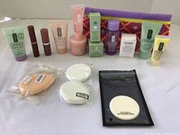 Full view of lot items showing skincare tubes and jars, lipsticks, boxed items, makeup sponges, and makeup bag on white surface.