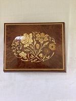 Closed rectangular wooden jewelry box with detailed floral inlay on the lid and golden border.