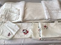 Assorted folded tablecloths and embroidered napkins on table displaying fabric texture and details