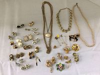 Full view of multiple vintage costume jewelry items spread on fabric including necklaces, earrings, and brooches with various shapes and colors.