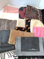 Lot overview showing multiple scarves and wraps of various colors and patterns with some folded and some stacked.