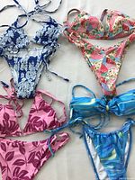 Four women's medium bathing suits in different colors and floral/abstract patterns on a flat surface.