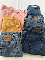 Photo showing a stack of eight women's jeans in various washes and colors including blue denim, mustard yellow, and pink.