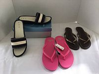 Lot of three women's sandals: One pair Nine West black/white slide sandals on box, one bright pink flip flop pair with tag, and one brown thong sandal pair with gold straps.