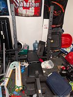 Wide view of the black padded adjustable bench press with grey barbell rack posts in cluttered basement