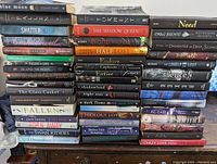 Photo showing large stack of fantasy and fiction books with visible titles such as Blue Moon, Shatter Me, Shadow Queen, Need, Wuthering Heights, and others