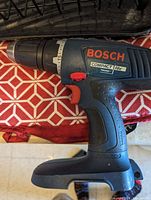 Bosch Compact 18V cordless drill with textured grip and red trigger, placed on patterned cloth.