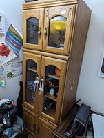Full front view of the oak-colored press wood cabinet showing upper glass doors, lower mixed glass and wood doors, decorative molding, and signs of wear.