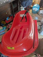 Red plastic child's sled placed on floor with strap and visible seating and footrest area.