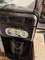 Front view of Hamilton Beach coffee maker showing control buttons, digital display, and glass carafe.
