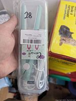 Front view of small hair straightener in original clear plastic packaging, showing light blue device with power button and attached white cord.