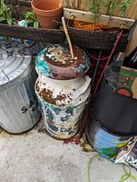 Vintage metal milk can with visible rust and flaking paint next to a trash bin and planter.