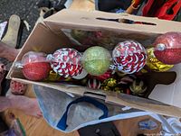 Top view of the ornaments inside the box showing a variety of red, green, gold, and white patterned round plastic ornaments.