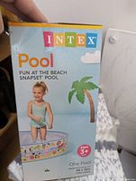 Box front showing a young child sitting in the pool with the pool's colorful beach-themed design.