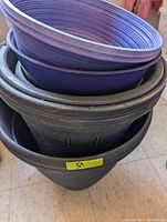 Stacked assortment of purple and black plastic pots and planters of various sizes and textures, showing rims and interiors.