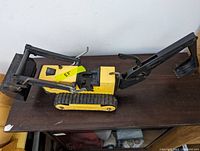 Side view of vintage Tonka yellow excavator toy on a wooden surface, shows extendable arm and black digging bucket.