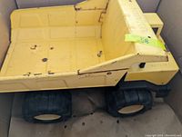 Side view of yellow Tonka dump truck showing the dump bed and part of the cab with wear and rust spots.