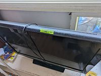 Full view of the black flat screen TV leaning against a wall with visible screen scratch and power cord wrapped around it.