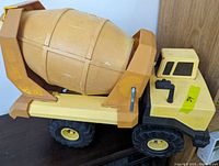 Side view of the yellow and orange-brown plastic cement drum attached to the yellow truck body showing overall color and condition