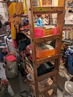 Wooden utility shelf from side angle showing four shelves and metal bracing on sides. Shelf currently holds several items but they are not included in sale.