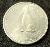 Front side of the 1867-1967 Canadian silver 50 cents coin depicting a howling wolf and inscriptions.